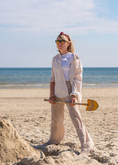 Young pretty woman having fun on beach. Builds tower of sand, digs sand with child shovel. Fun,...