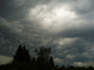 Stormy sky with gray and dense threatening rainy clouds and horizon with dark trees on spring season. Topics: meteorology, natural environment, climate, storm, atmosphere