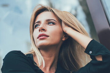 Fototapeta premium Below view of pondering woman dressed in stylish black shirt thougthful looking away and thinking on ideas, attractive hipster girl in casual clothing lost in thoughts during rest time on city bench