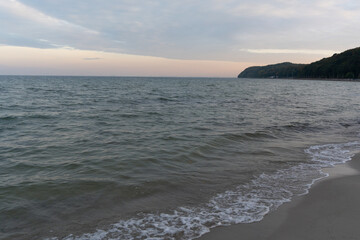 A warm summer sunset over the sea, with vibrant colors reflected on the calm water. Gentle waves softly kiss the sandy beach, creating a sense of tranquility.