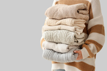 Woman holding stack of different warm clothes against light wall