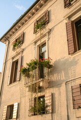 Fototapeta premium Cute small balcony with red flowers on yellow building in sunset, Verona, Italy