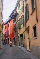 Fototapeta premium Colorful street houses in Verona, Italy with a person riding on a scooter