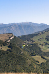 One person paragliding into green mountains with bright blue sky, Italy