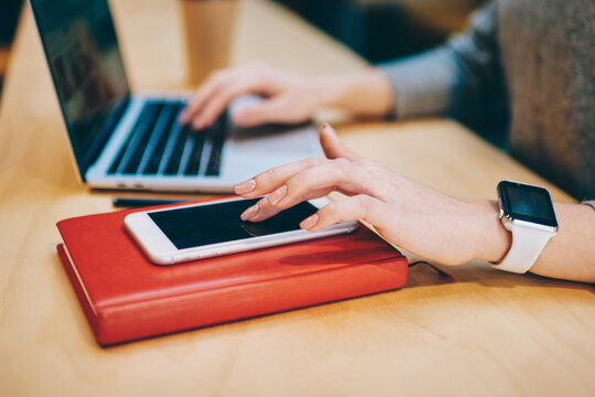 Cropped image of female hand searching sms message on new smartphone gadget standing on red textbook for education, skilled remote worker checking notification received on modern mobile phone