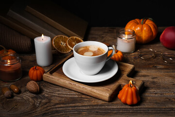 Burning candles with pumpkin, apple, dried orange, books and cup of coffee on wooden table