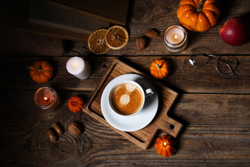 Burning candles with pumpkins, apple, dried orange, books and cup of coffee on wooden table