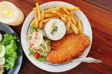 Classic serving of fish and chips with crispy fries, fresh salad, and tartar sauce on the side, garnished with a slice of lemon.