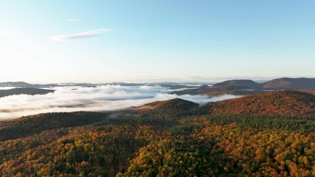 Time-lapse of rolling hills and colorful autumn forests blanketed by mist, with a clear sky and soft clouds moving over the landscape.
