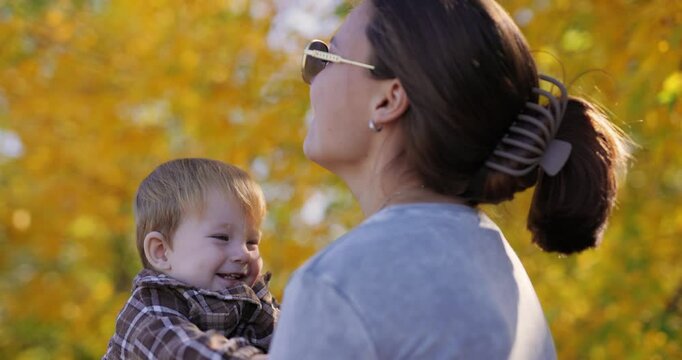 Slow motion, a mom holding and throwing a little happy son at autumn park