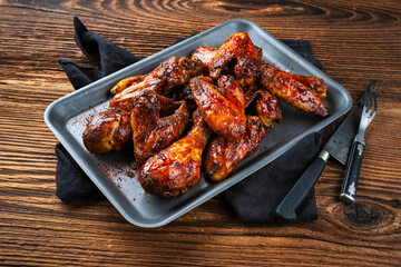 Authentical barbecue chicken wings and drumsticks with hot chili sauce as marinade served as close-up in a rustic backing sheet with copy space