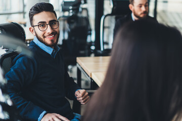Portrait of caucasian smiling man management expert in optical spectacles for vision correction looking at camera while sitting at office desktop and collaborating with male and female partners