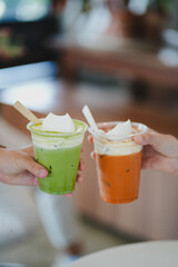 Selective focus hands of teenage girls holding glass of ice thai tea and ice matcha green tea...