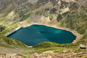 Bergsee mit Staumauer gefüllt mit türkis blauem Wasser 