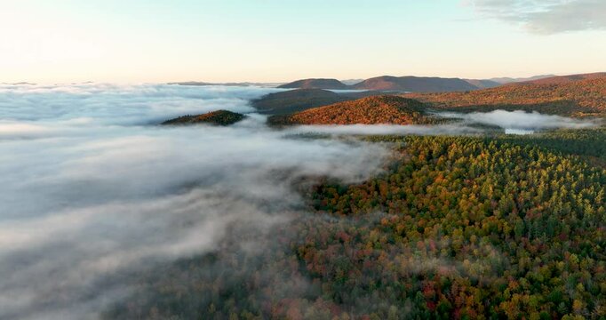 Aerial view of a mountain range covered in vibrant fall foliage, with mist and fog drifting over the colorful forested hills, capturing the beauty of the autumn season.