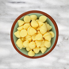 Top view of a small bowl filled with white baking chips isolated on a gray marble background.
