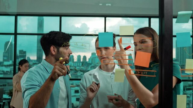 Happy businesspeople pointing at glass wall while standing with confident. Group of businesspeople writing at while standing at transparent board with business idea, strategy, planning. Tracery
