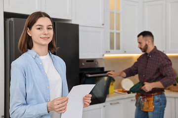 Obraz premium Smiling woman with sheet of paper and repairman fixing oven in kitchen, selective focus