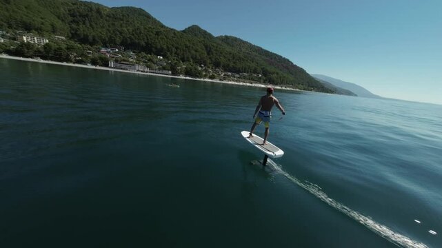 a sporty man learns to ride a hydrofoil among the beautiful blue sea against the background of green mountains