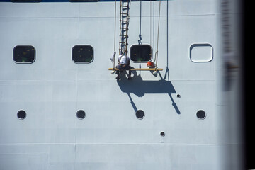Homem pendurado em cordas pintando navio