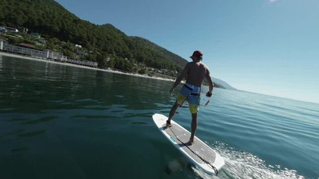 a sporty man learns to ride a hydrofoil among the beautiful blue sea against the background of green mountains
