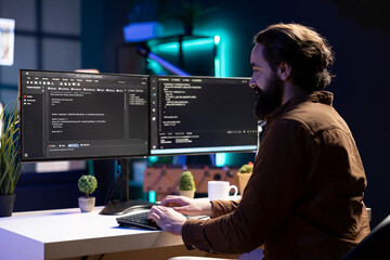 Smiling IT professional working from home developing software in Java programming language using desktop PC. Happy developer in apartment writing lines of binary code on computer using keyboard