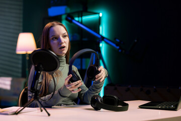 Young influencer in home studio films headphones comparison video review for audience, recording with professional microphone to accurately capture sound, hosting technology internet show for fans