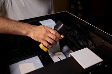 A man cleans a computer case with a vacuum in a bright room, stressing workspace tidiness