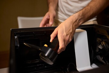 A man cleans a computer case with a vacuum in a bright room, stressing workspace tidiness