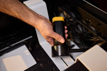 A man cleans a computer case with a vacuum in a bright room, stressing workspace tidiness