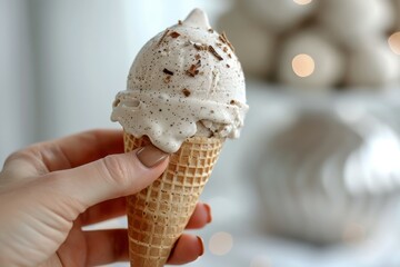 A close-up of a female hand holding a vanilla ice cream cone with sprinkles on a white background, perfect for summer-themed designs