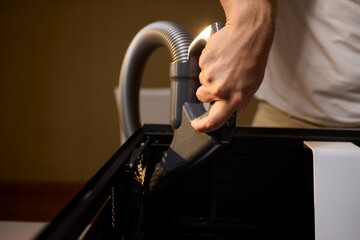 A man cleans a computer case with a vacuum in a bright room, stressing workspace tidiness
