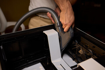 A man cleans a computer case with a vacuum in a bright room, stressing workspace tidiness