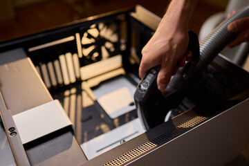 A man cleans a computer case with a vacuum in a bright room, stressing workspace tidiness