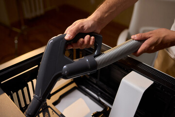 A man cleans a computer case with a vacuum in a bright room, stressing workspace tidiness