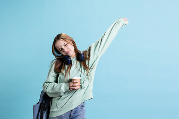 Joyous teenager enjoying music, dancing with headphones, drinking coffee cup. Happy woman consuming...