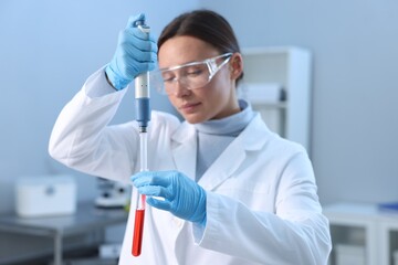 Naklejka premium Laboratory testing. Doctor dripping blood sample into test tube indoors