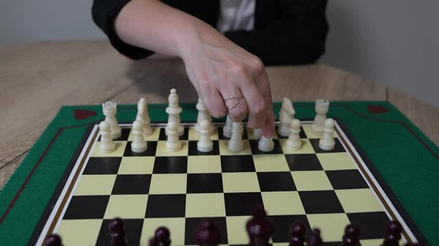 A woman is playing a game of chess with a man. The woman is wearing a black jacket and white shirt