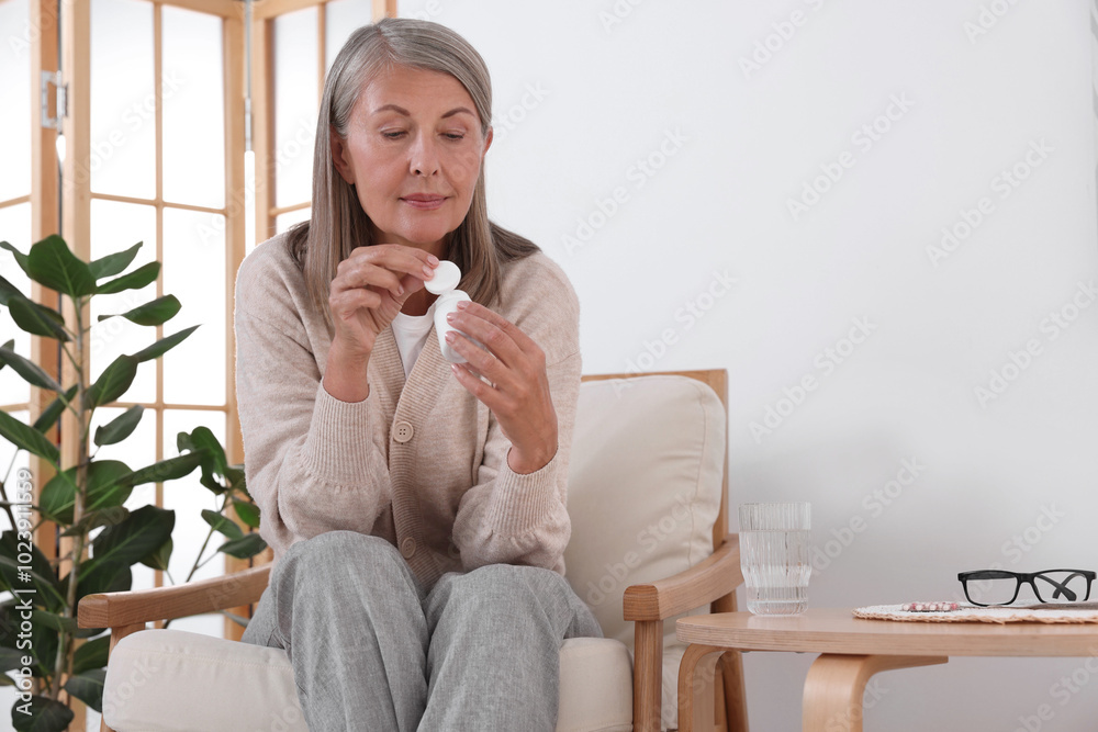 Sticker Senior woman with bottle of pills in armchair at home