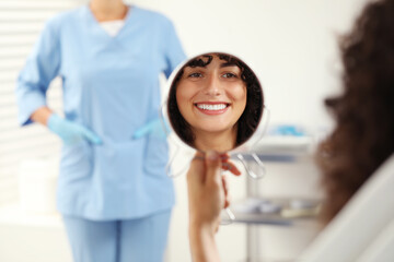 Obraz premium Patient looking in mirror and doctor in clinic, selective focus. Dental veneers