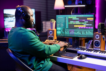 Young songwriter twisting pre amp knobs and mixing sounds with a console, looking at record settings on a digital software. Artist musician producing new tracks, stereo gear in home studio.