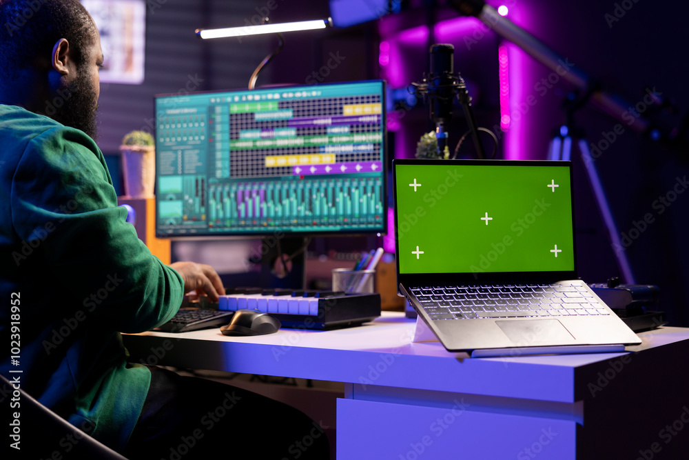 Poster professional artist operating on daw software in home studio, using a greenscreen layout next to him