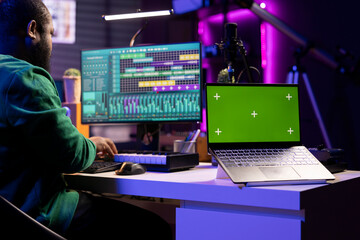 Professional artist operating on daw software in home studio, using a greenscreen layout next to...