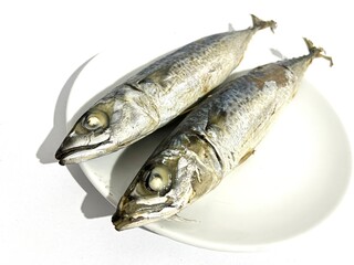 Two salted sardine or cue fish with shiny silver skin on a round ceramic plate isolated on white...