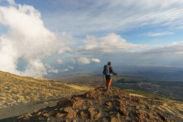 Obraz premium Hiking person looking at view of volcanic landscape of Mount Etna with black lava and yellow grass on partly cloudy winter day, Catania, Sicily, Italy
