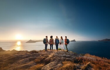 Fototapeta premium Four people stand on a cliff looking at a view of a sunset over the ocean.