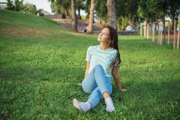 Fototapeta premium Portrait of cute charming lady sitting lend ground fresh green grass enjoy sun nature harmony student resting from city crowd people wear t-shirt jeans colorful park outdoors