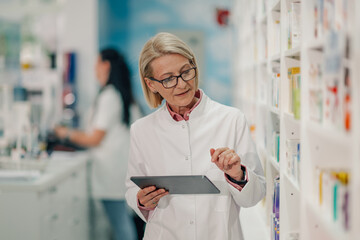 Senior pharmacist using digital tablet while checking medicine stock