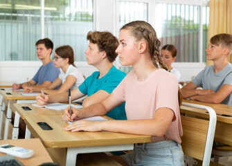 Fototapeta premium Teenagers sitting in class room and listening. Girl sitting in foreground.