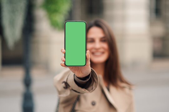 Smiling woman holding smartphone with green screen outdoors - Powered by Adobe